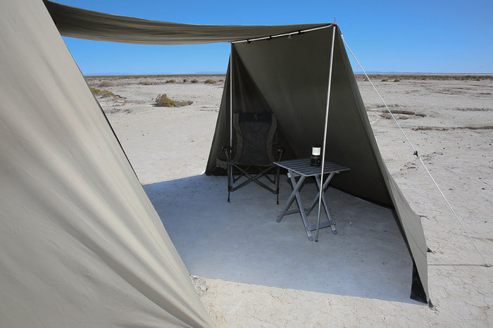 Spacious outdoor shelter with a beige tarp, folding chair, and side table, ideal for camping or relaxing.
