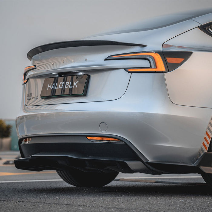 A close-up of a silver Tesla Model 3 Highland features a Carbon Fiber Rear Spoiler from HALOBLK Store, showcasing its taillights and a HALO BLK license plate while parked on the street.