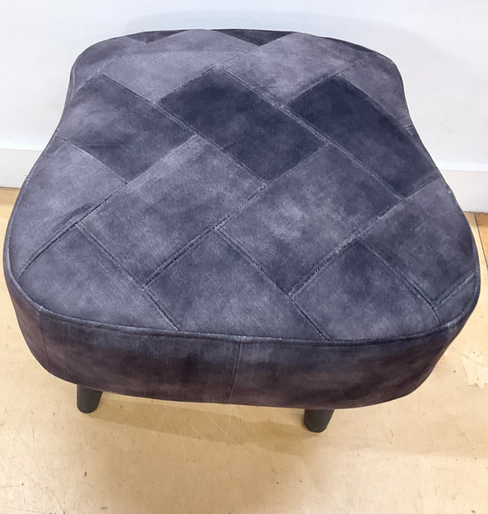 Gray quilted ottoman on a light wooden floor with a white wall background
