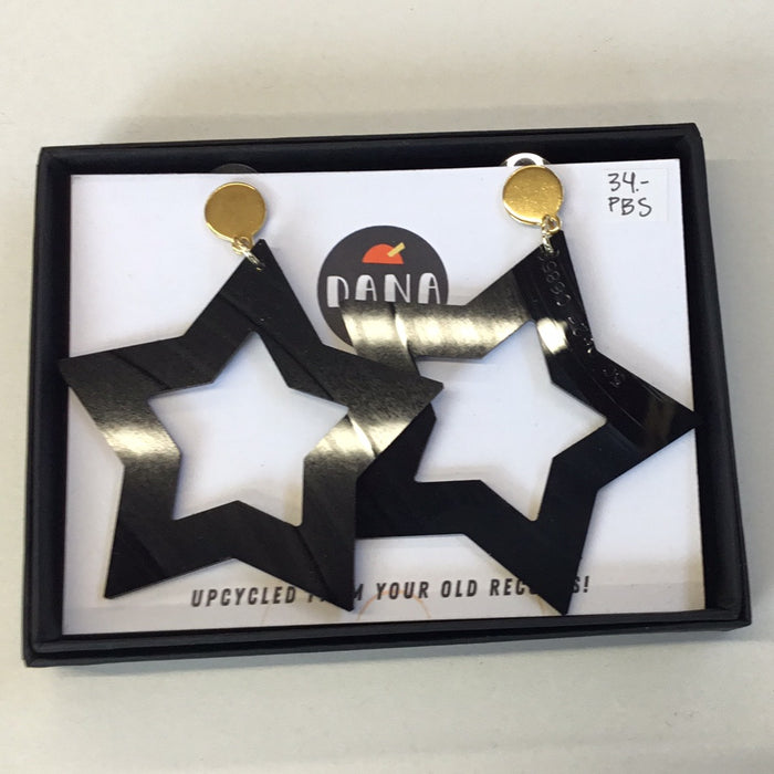 A pair of large black star-shaped earrings with gold studs, presented in a box with a brand tag.
