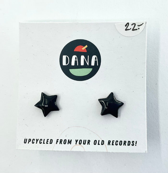 A pair of black star-shaped stud earrings on a white card with the brand name 'DANA' at the top. The card indicates the earrings are made from upcycled vinyl record jewellery.