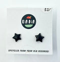 A pair of black star-shaped stud earrings on a white card with the brand name 'DANA' at the top. The card indicates the earrings are made from upcycled vinyl record jewellery.