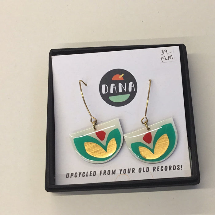 A pair of earrings designed with geometric shapes in white, turquoise, red, and bronze colors, presented on a black display card with the brand name 'DANA' at the top.