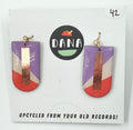 A pair of earrings made from upcycled vinyl records, predominantly red and purple in color, with a gold-colored bar at the top, displayed on a white background with the brand name 'DANA' above.