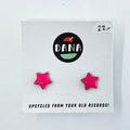 A pair of pink star-shaped stud earrings on a white card with the brand name 'dana' at the top. The card has the text 'upcycled from your old records!'