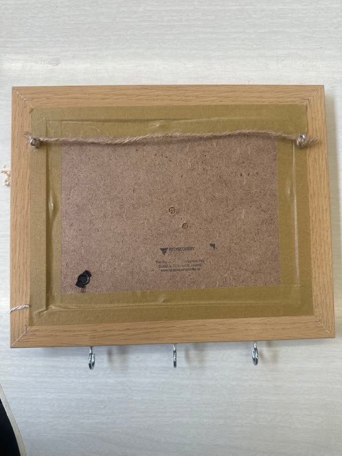 The back view of a square picture frame with a light oak wood border, a brown cardboard backing, and a gold-colored inner liner, shown on a white textured background.