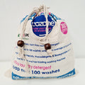 A beige drawstring bag labeled 'Ecozone' with a blue label that reads '300g', '100 washes', and 'Natural & Friendly'. There are also text highlights about the product being a top-loading washing machine, not being a skin irritant, and being sourced from recyclable materials.
