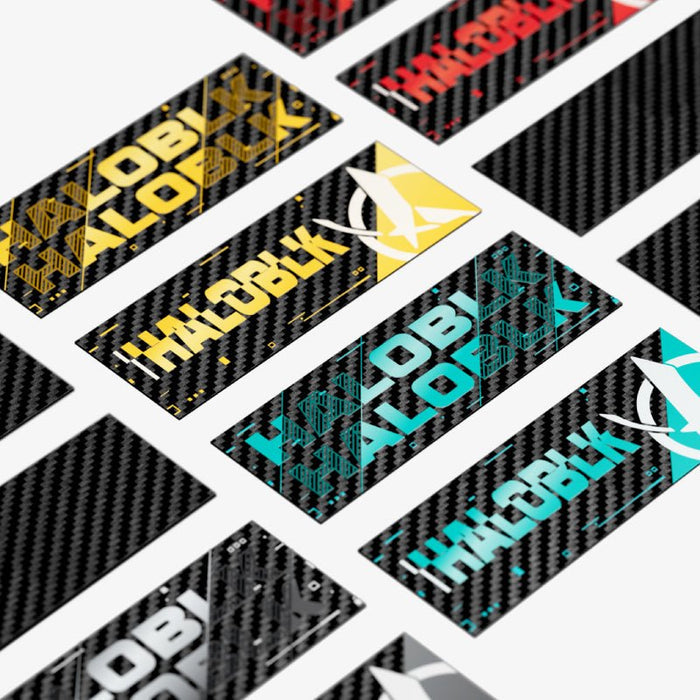 HALOBLK Carbon Fiber Emblem – HALO EFFECT Series by HALOBLK Store shown in yellow, turquoise, red, and white with circuit patterns on a carbon fiber background, arranged diagonally on a white surface.