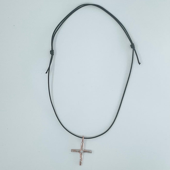 A black adjustable cord necklace with a small rose gold cross pendant, displayed on a light gray background.