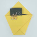 A pair of rose gold double hoop earrings with small clear crystal accents, presented on a yellow envelope with a black card that reads 'Since 2020'.