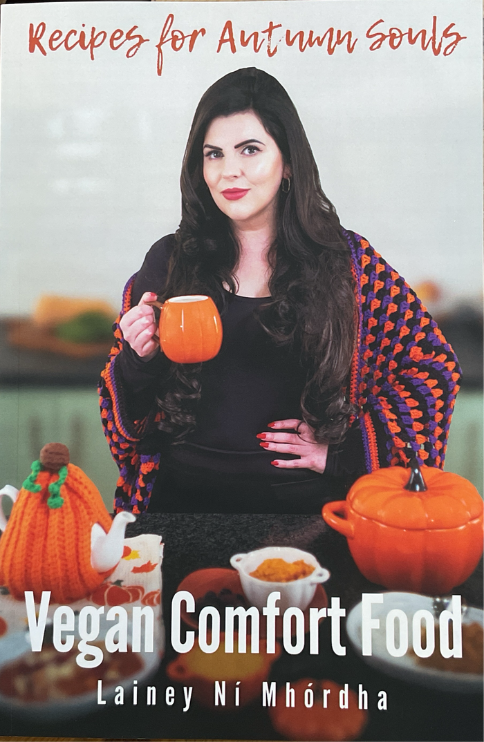 A book cover for 'Recipes for Autumn Souls' featuring a woman holding a mug with a colorful blanket in the background, and various kitchen items like pumpkins and a teapot.