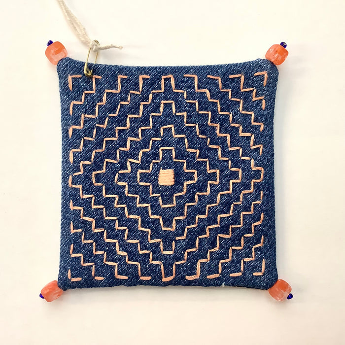 Decoratively stitched denim coaster with a geometric pattern and beads on each corner