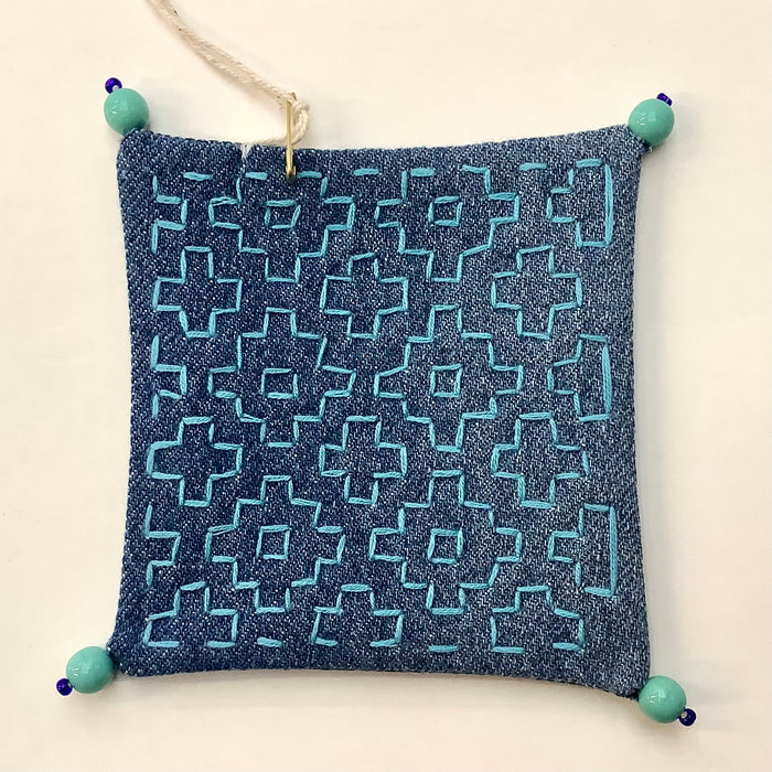 Coaster made from upcycled jeans with blue geometric embroidery and blue beads on each corner