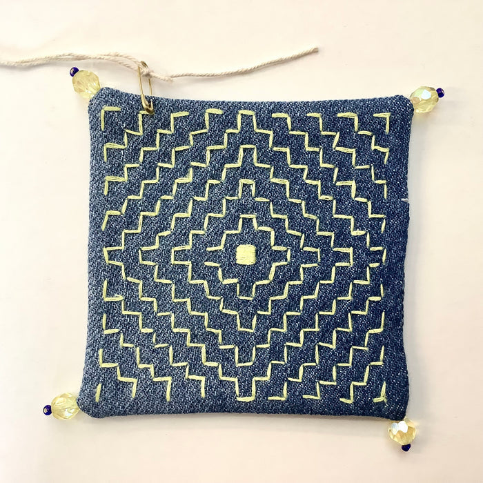 Denim coaster with yellow geometric embroidery and yellow beads on each corner