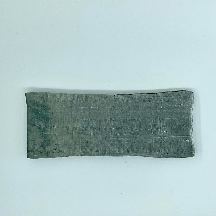 A gray silk eye mask laid flat on a white background.
