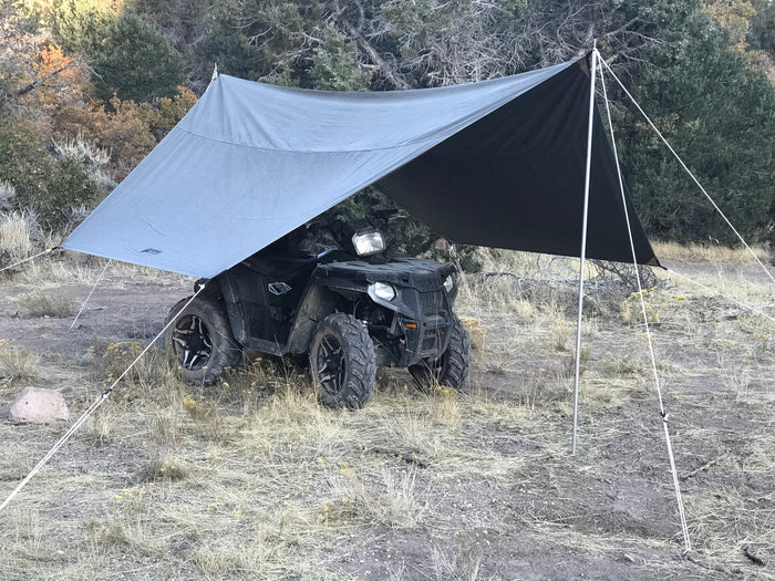 Durable outdoor tarp shelter in gray, providing shade for an ATV in a rugged, natural setting.