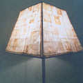 A lamp shade made out of paper tea bags with a beige and brown color, featuring a unique geometric shape and placed on a stand.