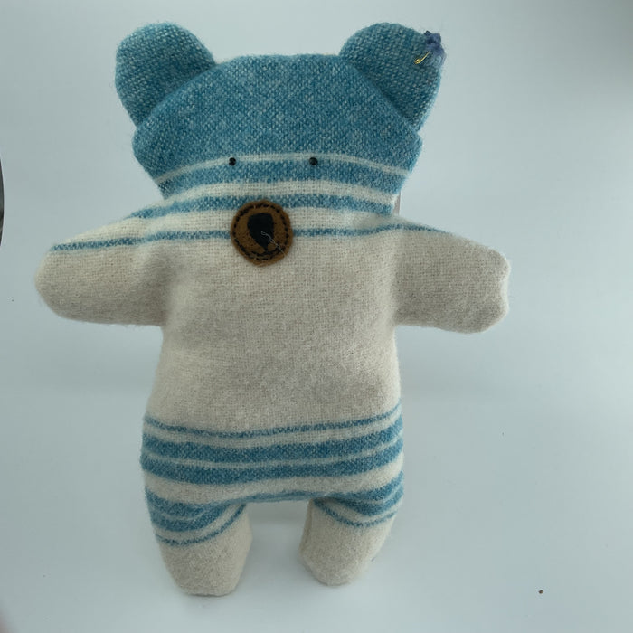 Stuffed toy bear with blue and white striped outfit on a light gray background