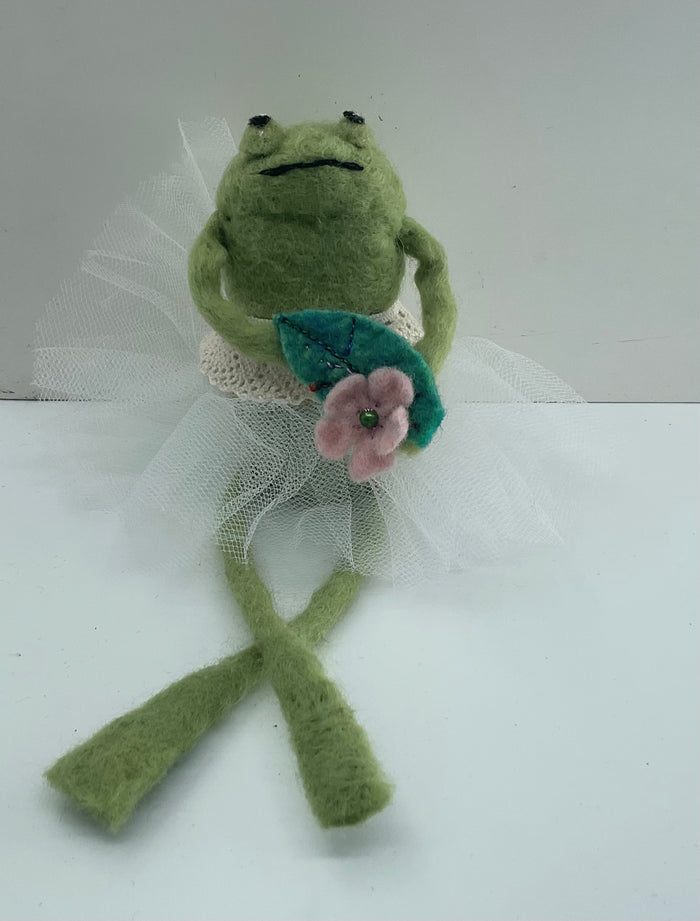 Green frog plush toy in a white dress with a flower on a white background