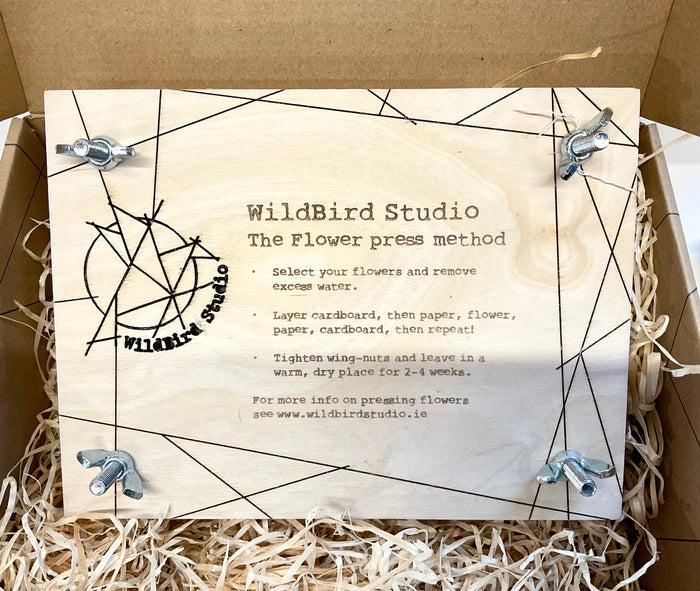 Flower press with WildBird Studio branding and instructions on a cardboard background
