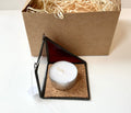 Candle in a geometric holder with a cardboard box containing straw on a white background